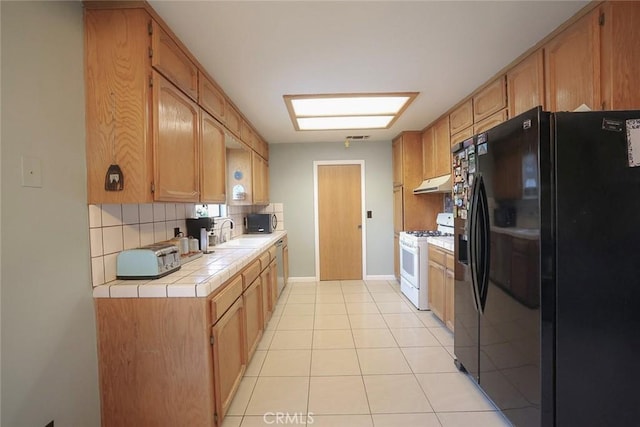 kitchen with tile countertops, backsplash, white range with gas stovetop, light tile patterned floors, and black refrigerator with ice dispenser