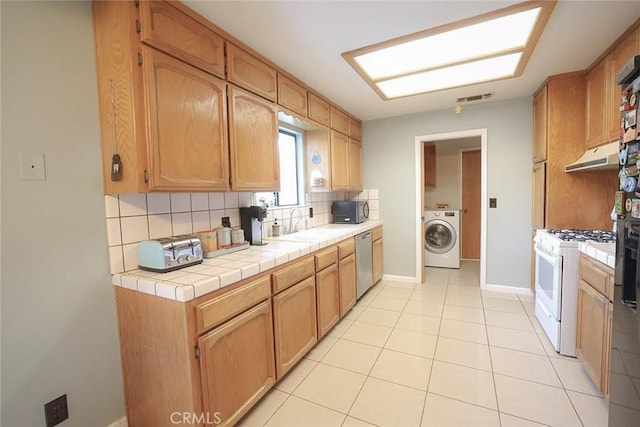 kitchen featuring washer / dryer, white range with gas stovetop, tasteful backsplash, tile countertops, and stainless steel dishwasher