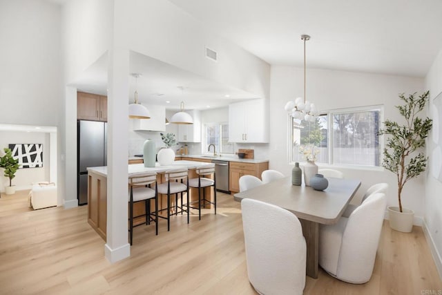 dining space with high vaulted ceiling, a chandelier, sink, and light hardwood / wood-style flooring