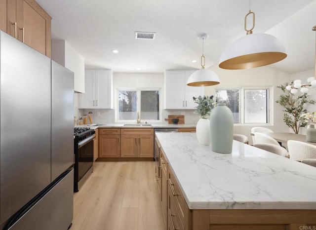 kitchen with sink, stainless steel refrigerator, gas range oven, white cabinets, and decorative light fixtures