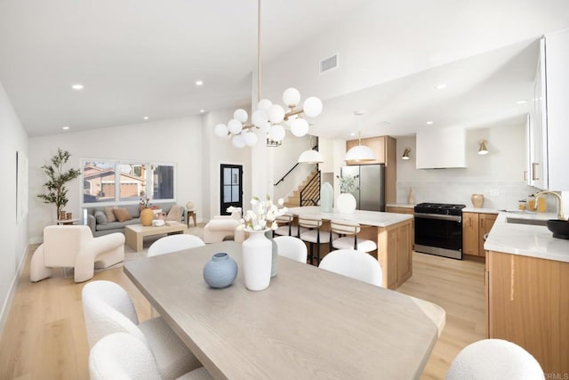 dining space with lofted ceiling, sink, light hardwood / wood-style floors, and an inviting chandelier