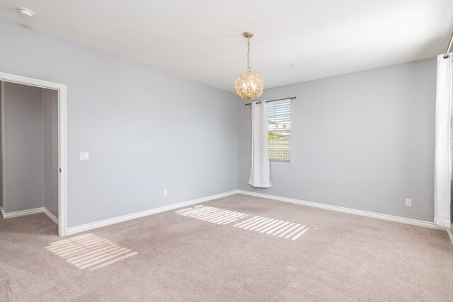 spare room featuring an inviting chandelier and carpet flooring