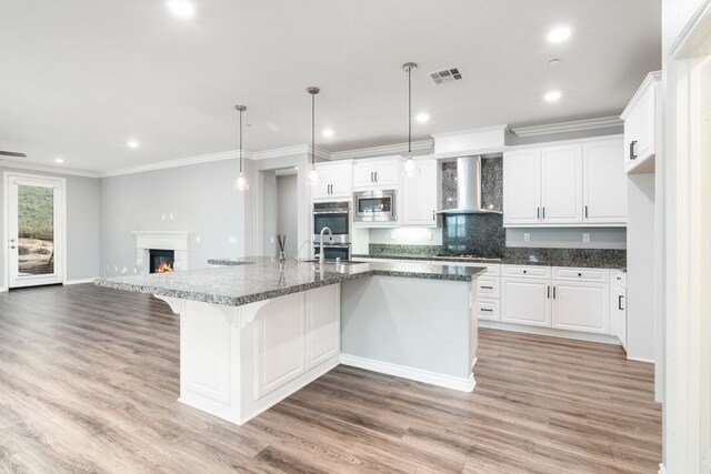 kitchen with a large island, wall chimney range hood, stainless steel appliances, white cabinets, and hanging light fixtures