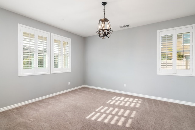 spare room featuring an inviting chandelier and carpet flooring