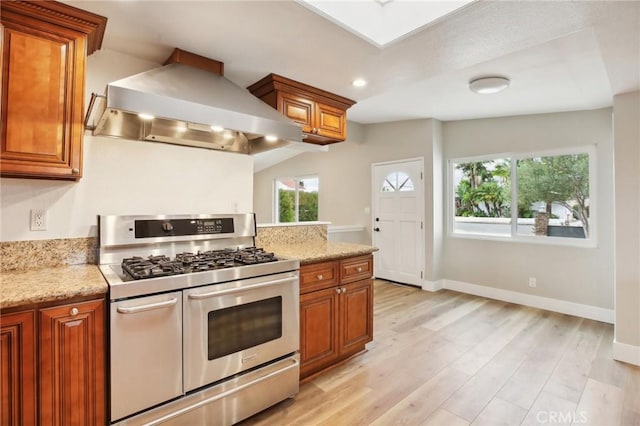 kitchen with range with two ovens, light stone countertops, wall chimney range hood, and light hardwood / wood-style flooring