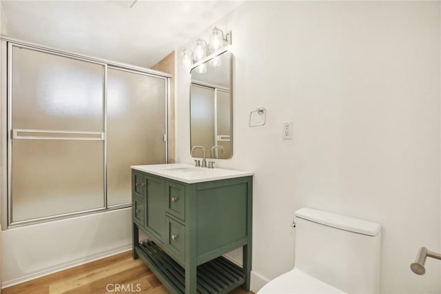 full bathroom featuring hardwood / wood-style flooring, vanity, toilet, and combined bath / shower with glass door