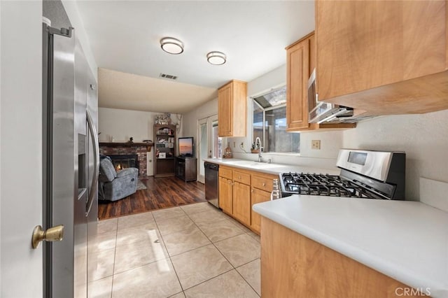 kitchen with light brown cabinetry, sink, light tile patterned floors, stainless steel appliances, and a fireplace