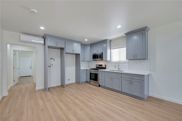 kitchen with gray cabinetry, appliances with stainless steel finishes, sink, and an AC wall unit