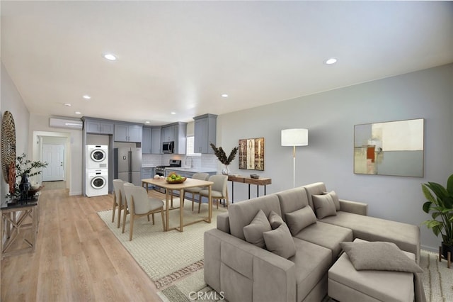 living room featuring stacked washing maching and dryer, light hardwood / wood-style floors, and a wall unit AC