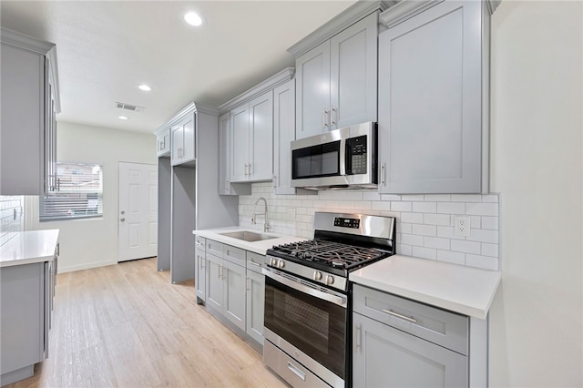 kitchen with gray cabinets, appliances with stainless steel finishes, tasteful backsplash, sink, and light hardwood / wood-style floors