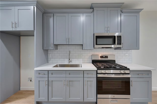 kitchen featuring sink, gray cabinets, appliances with stainless steel finishes, tasteful backsplash, and light hardwood / wood-style floors