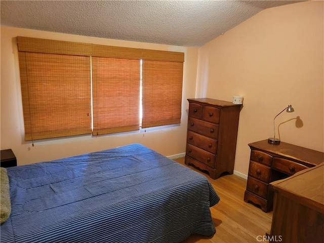 bedroom featuring vaulted ceiling, light hardwood / wood-style floors, and a textured ceiling