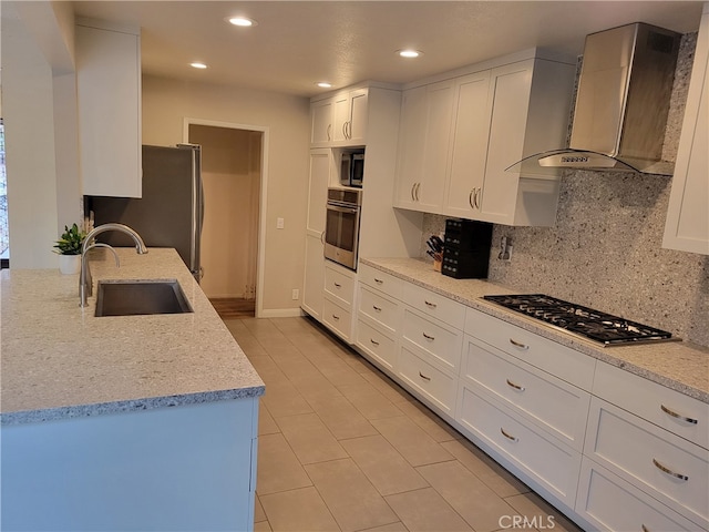 kitchen featuring sink, appliances with stainless steel finishes, white cabinetry, light stone counters, and wall chimney exhaust hood