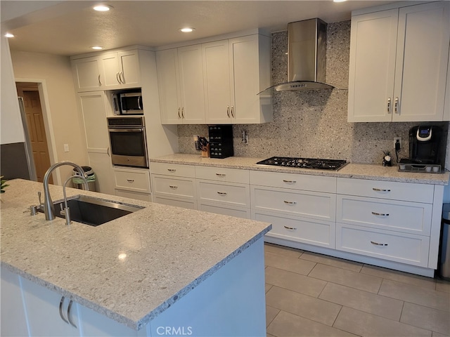 kitchen with sink, appliances with stainless steel finishes, light stone counters, white cabinets, and wall chimney exhaust hood