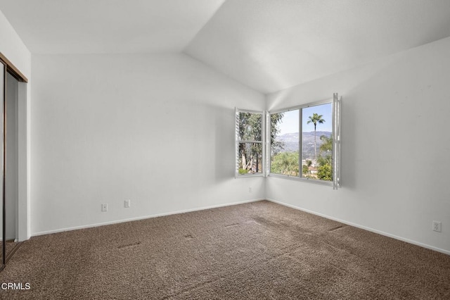 carpeted spare room featuring baseboards and vaulted ceiling