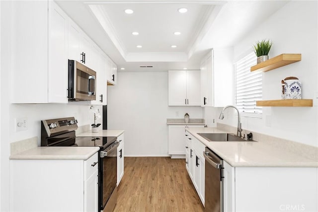 kitchen with a raised ceiling, sink, white cabinets, stainless steel appliances, and light hardwood / wood-style flooring