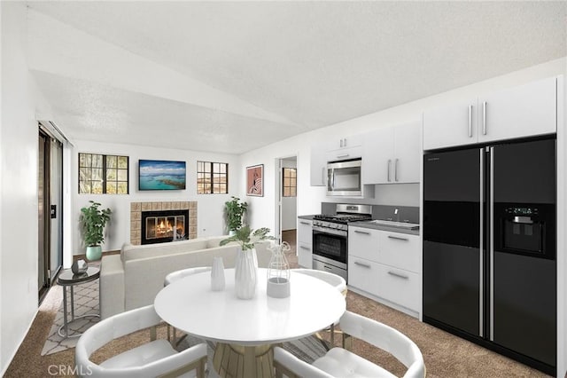 kitchen with white cabinetry, appliances with stainless steel finishes, light carpet, and a fireplace