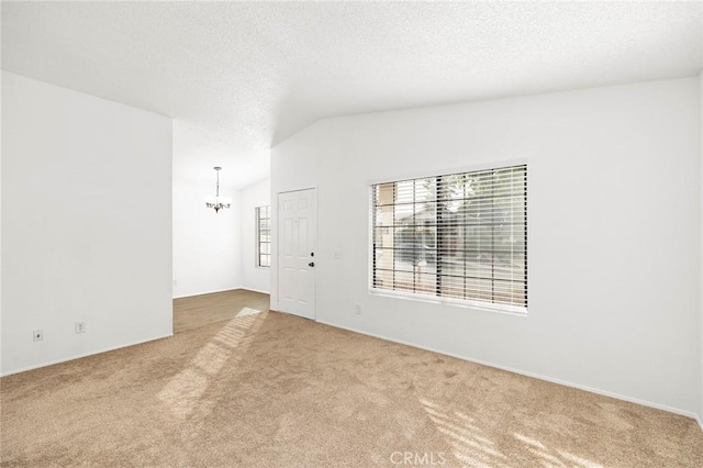 empty room with vaulted ceiling, light colored carpet, a notable chandelier, and a textured ceiling