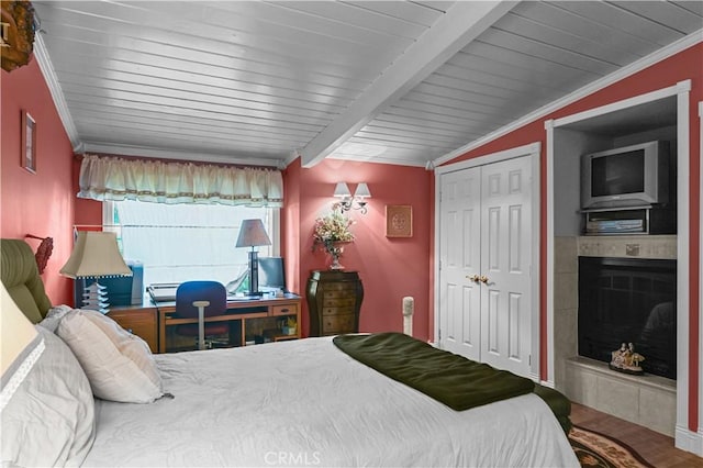 bedroom with vaulted ceiling with beams, crown molding, wooden ceiling, a closet, and a tiled fireplace