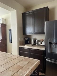 kitchen featuring dark brown cabinetry, stainless steel fridge with ice dispenser, and tile countertops