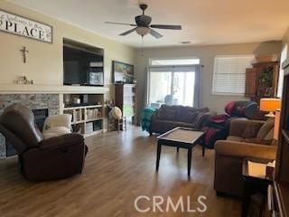 living room featuring ceiling fan, a stone fireplace, and hardwood / wood-style floors