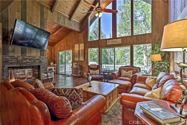 living room with wood ceiling, hardwood / wood-style flooring, beam ceiling, a stone fireplace, and wood walls