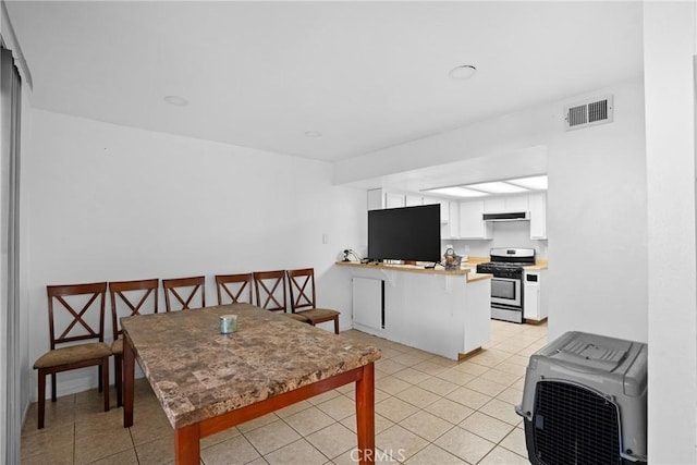 kitchen featuring white cabinetry, kitchen peninsula, light tile patterned floors, and stainless steel gas stove