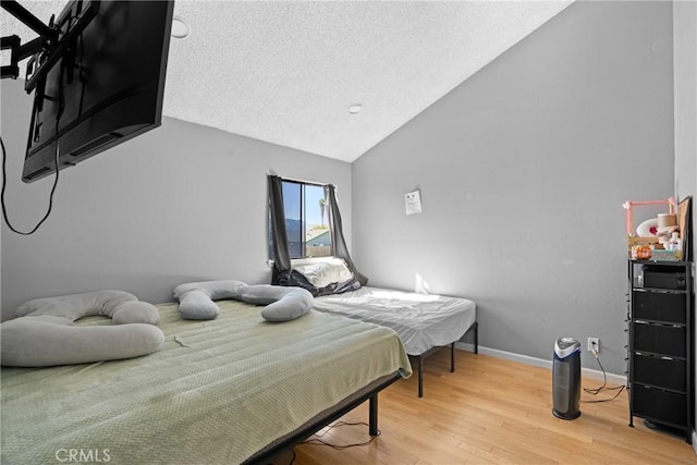 bedroom featuring hardwood / wood-style flooring, vaulted ceiling, and a textured ceiling