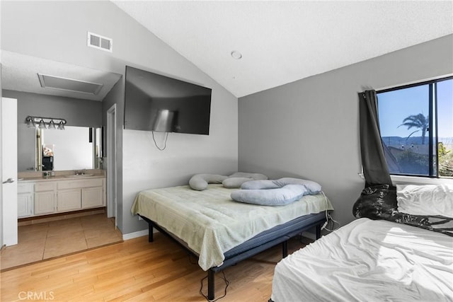 bedroom featuring ensuite bath, lofted ceiling, sink, and light wood-type flooring