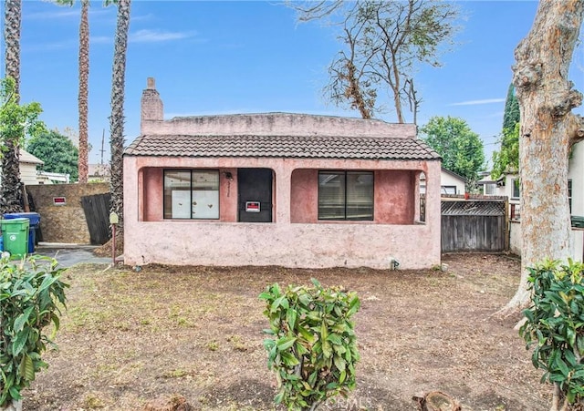 view of front of home with a tile roof, a chimney, fence, and stucco siding