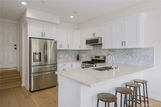 3822 Clayton Ave, Los Angeles, CA 90027 - kitchen featuring a peninsula, white cabinets, appliances with stainless steel finishes, light wood finished floors, and a sink