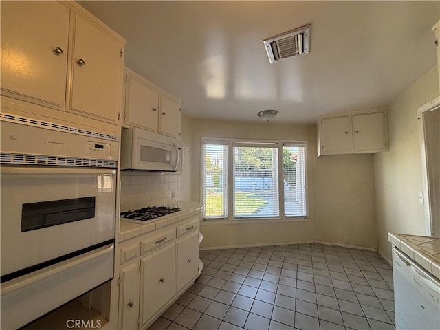 kitchen featuring tile countertops, tasteful backsplash, white cabinets, light tile patterned floors, and white appliances