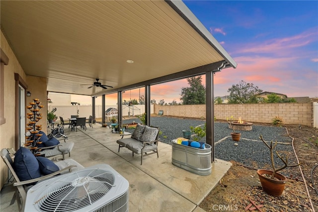 patio terrace at dusk with central AC unit, a fire pit, and ceiling fan