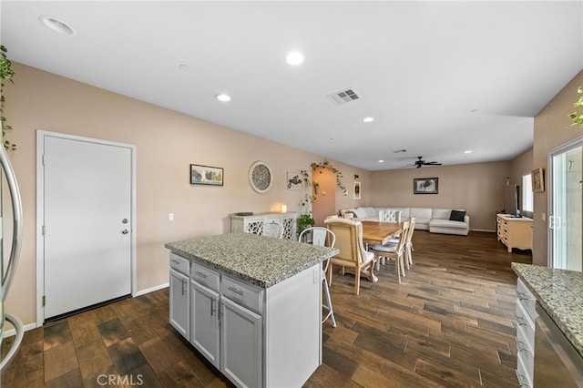 kitchen featuring dark hardwood / wood-style flooring, a center island, ceiling fan, and light stone counters