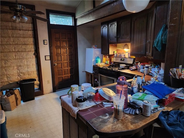 kitchen with dark brown cabinets, stainless steel range with gas cooktop, ceiling fan, and white fridge