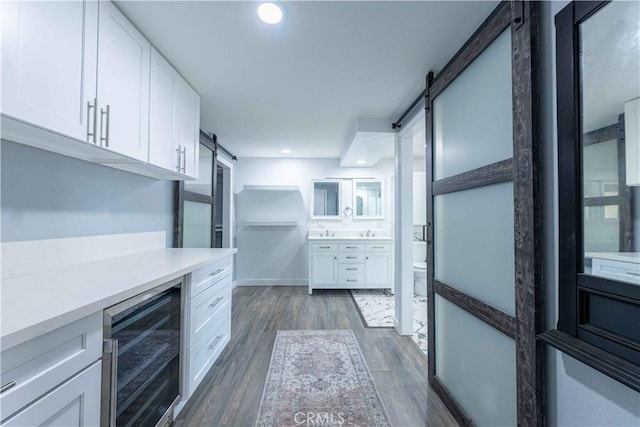 kitchen with wine cooler, white cabinetry, light stone counters, dark hardwood / wood-style flooring, and a barn door