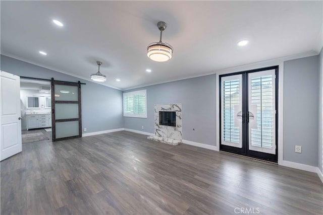 unfurnished living room featuring a fireplace, lofted ceiling, dark hardwood / wood-style flooring, ornamental molding, and a barn door