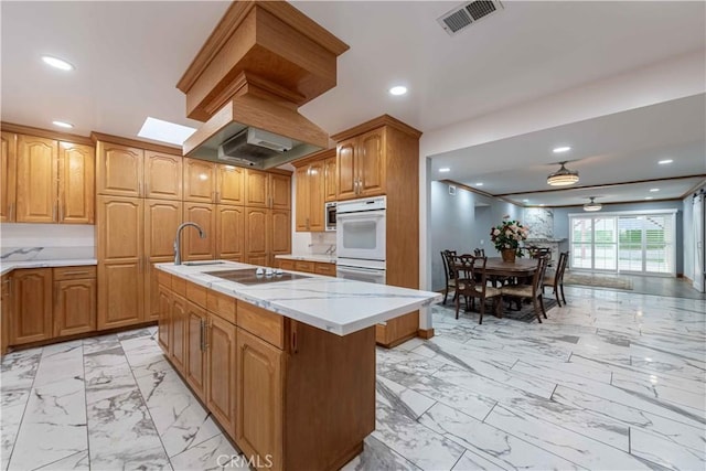 kitchen with black electric stovetop, white double oven, sink, and a kitchen island