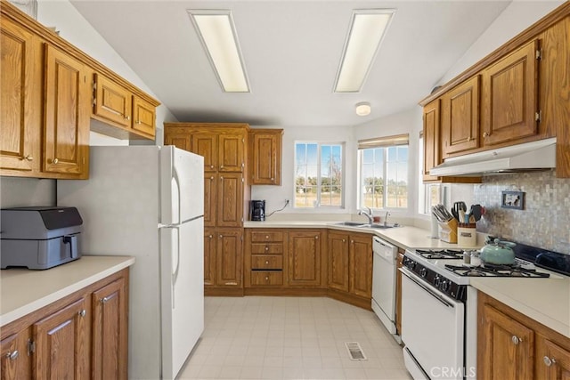 kitchen featuring under cabinet range hood, white appliances, a sink, light countertops, and brown cabinets