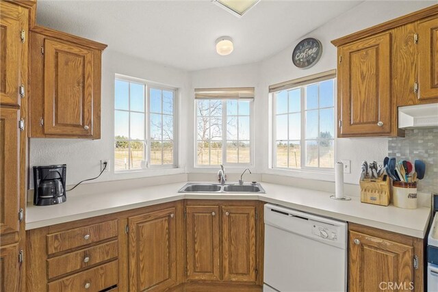 kitchen featuring brown cabinets, light countertops, backsplash, white dishwasher, and a sink