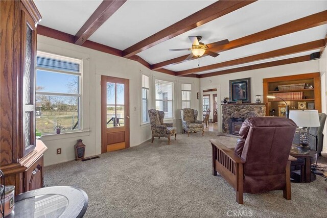 living area featuring light carpet, visible vents, a ceiling fan, a fireplace, and beam ceiling