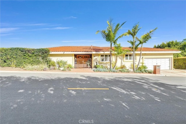 ranch-style home with a garage, driveway, a tiled roof, and stucco siding