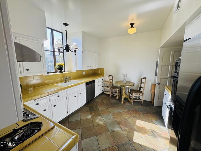 kitchen featuring stone tile flooring, a sink, fridge, dishwasher, and tile counters