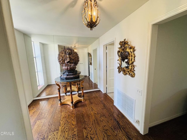 corridor featuring baseboards, wood finished floors, visible vents, and a chandelier