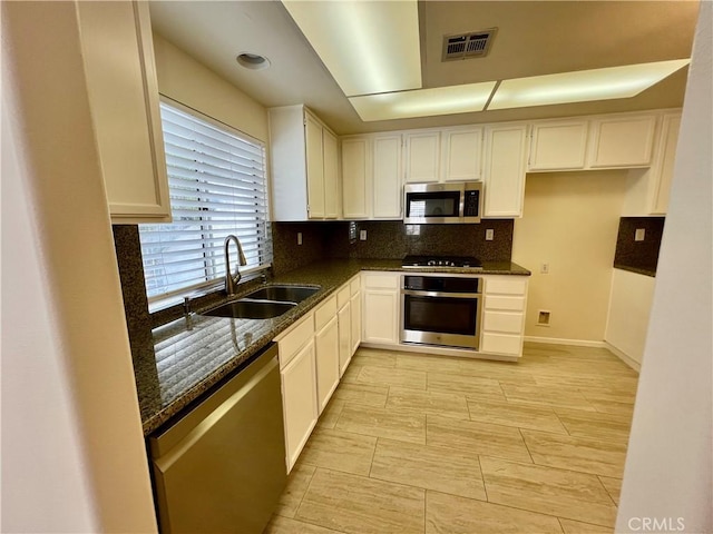 kitchen with stainless steel appliances, white cabinetry, sink, and dark stone countertops