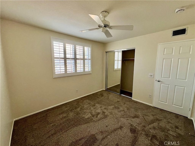 unfurnished bedroom with dark colored carpet, ceiling fan, and a closet