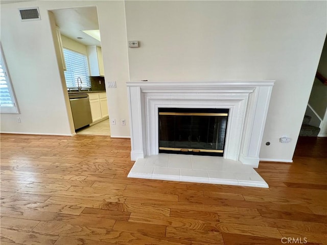 details with hardwood / wood-style floors, tasteful backsplash, dishwasher, sink, and a tiled fireplace