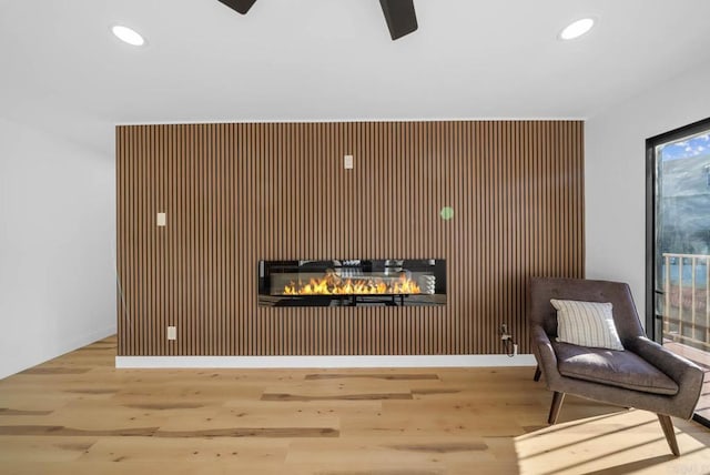 living area featuring hardwood / wood-style floors, ceiling fan, and wood walls