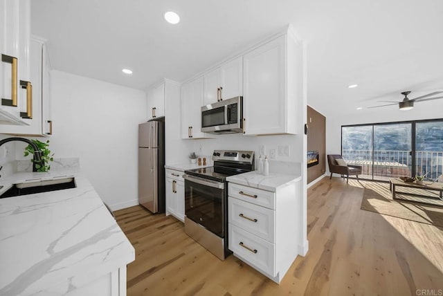 kitchen featuring sink, light wood-type flooring, appliances with stainless steel finishes, light stone countertops, and white cabinets