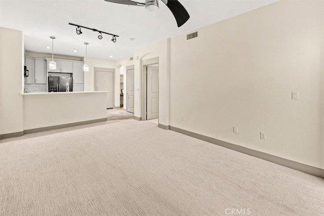 unfurnished living room with light colored carpet, track lighting, and ceiling fan